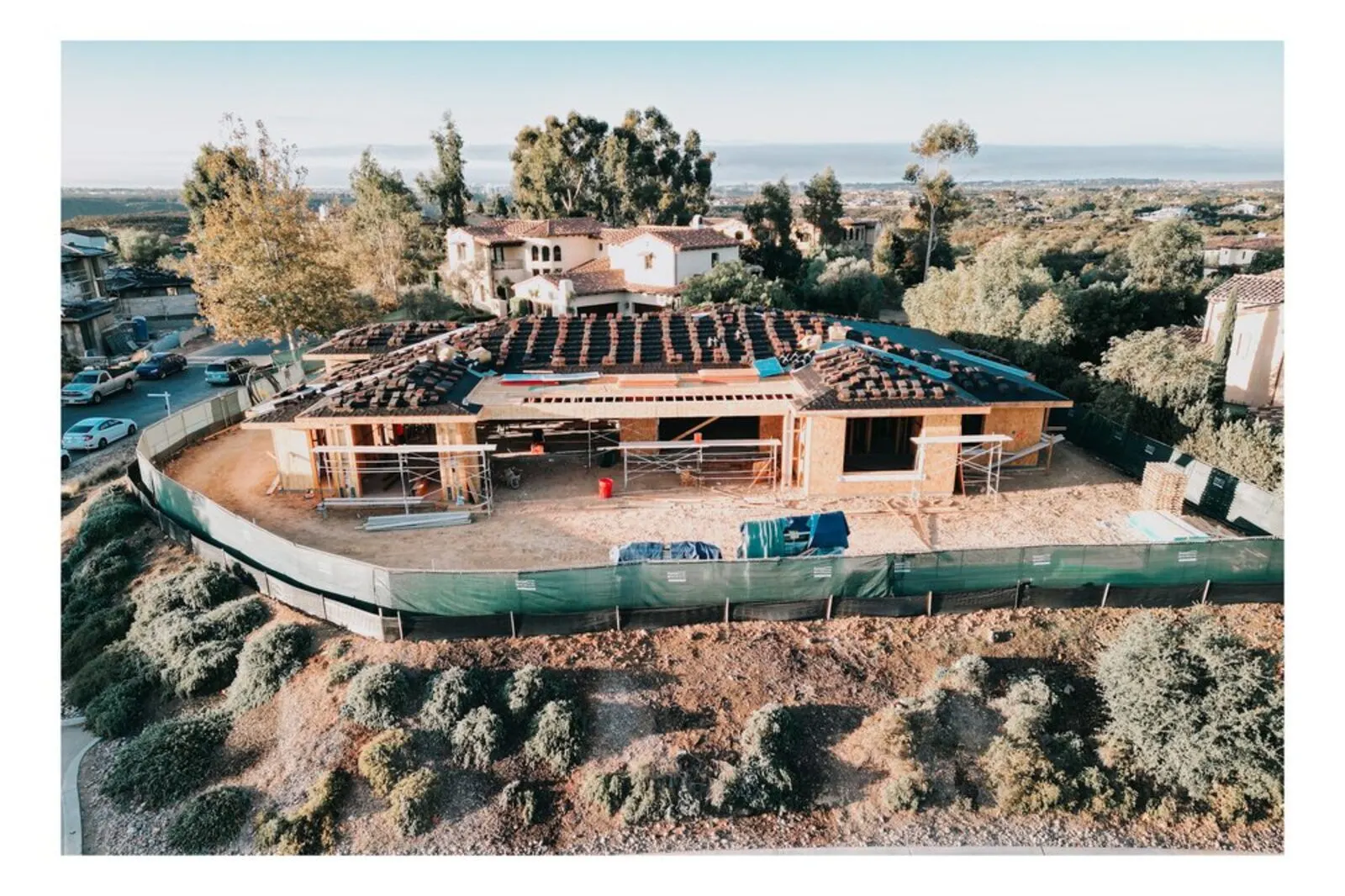 Aerial view of a custom home framing project with roof trusses complete, overlooking the San Diego coastline