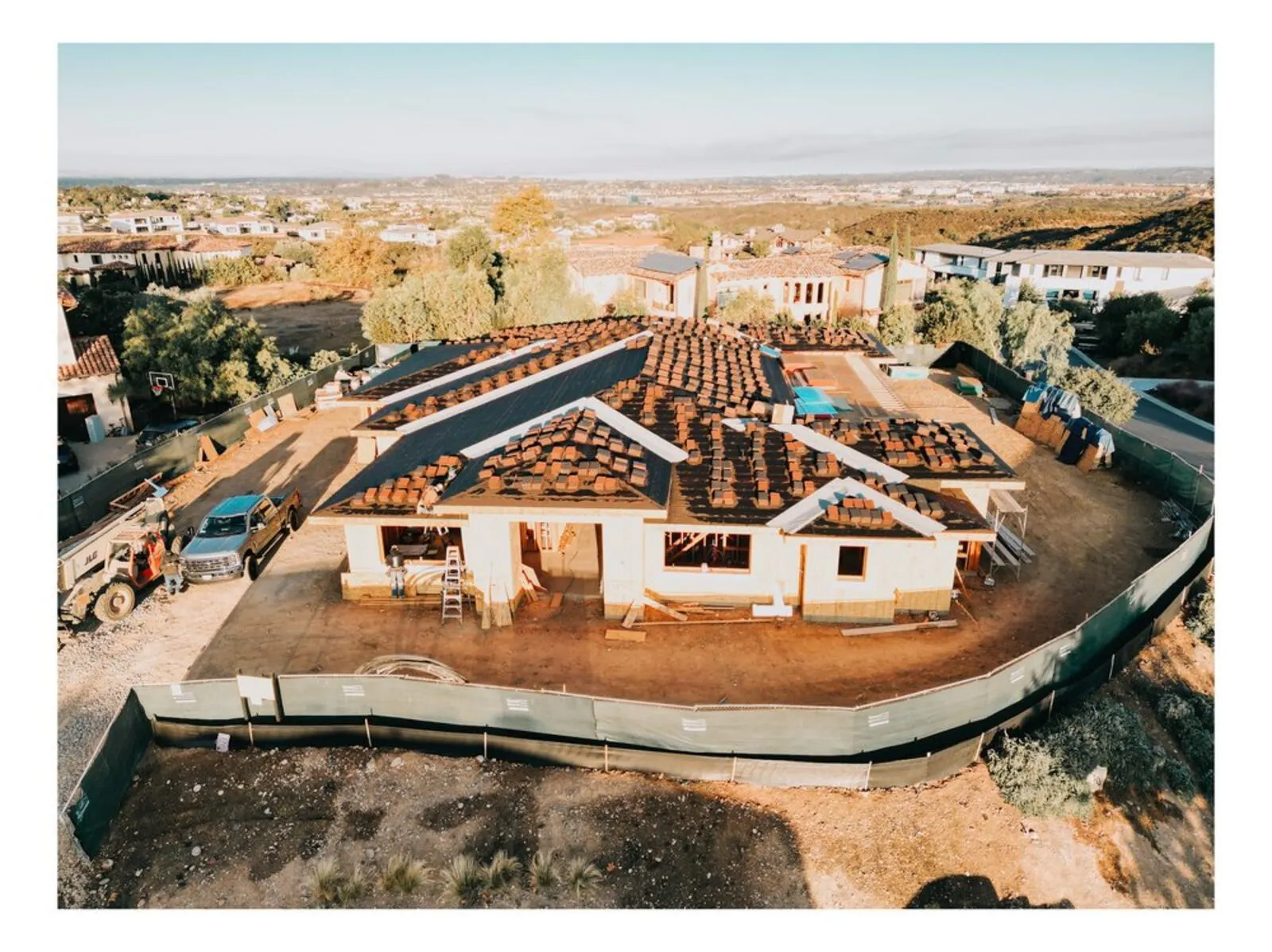 Custom home framing with roof trusses and sheathing nearing completion under a golden San Diego sunset